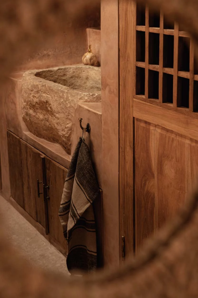 Warm kitchen with a stone basin, teak cabinetry and sculptural objects
