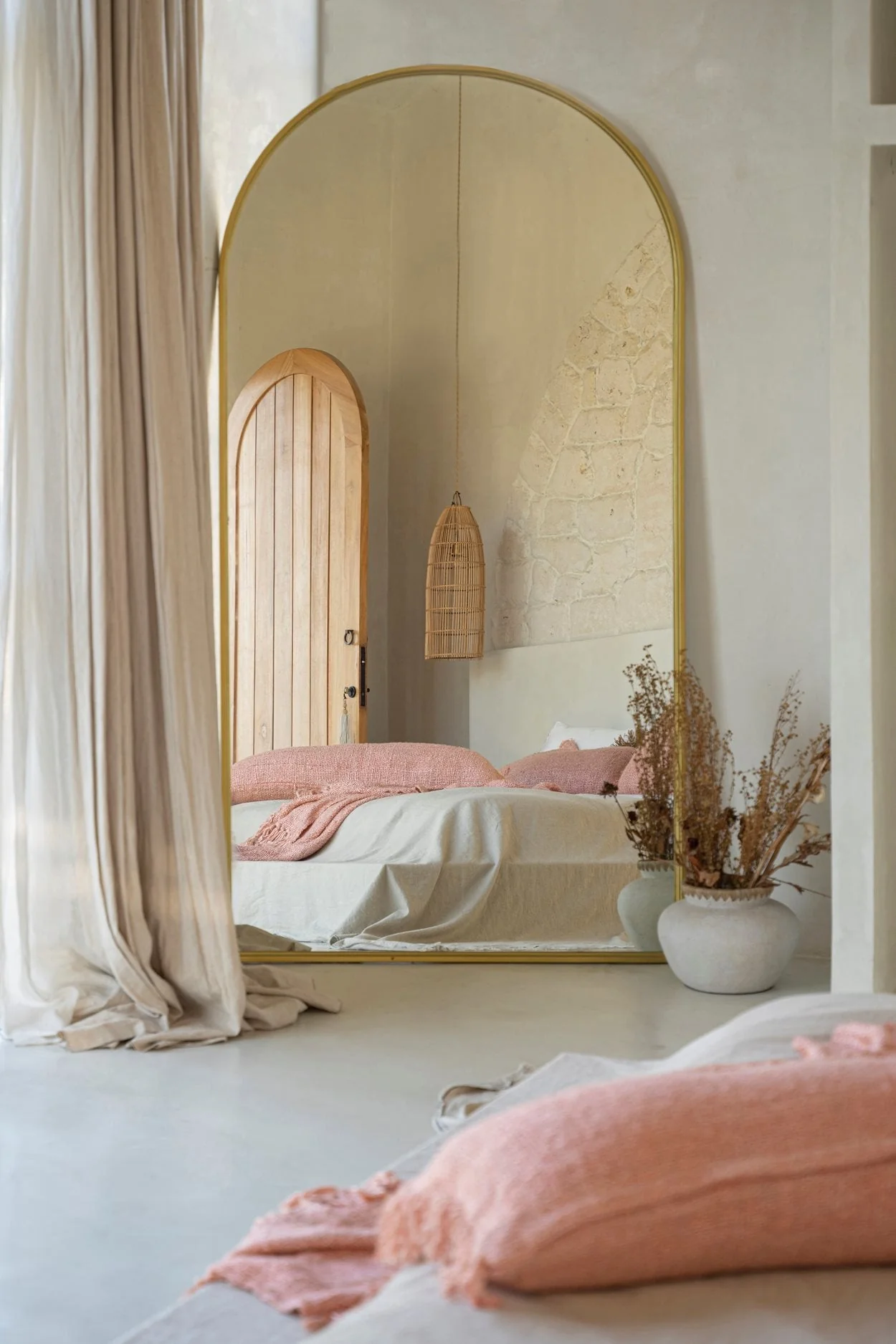 Serene bedroom with an arched mirror, linen curtains and a low timber bed