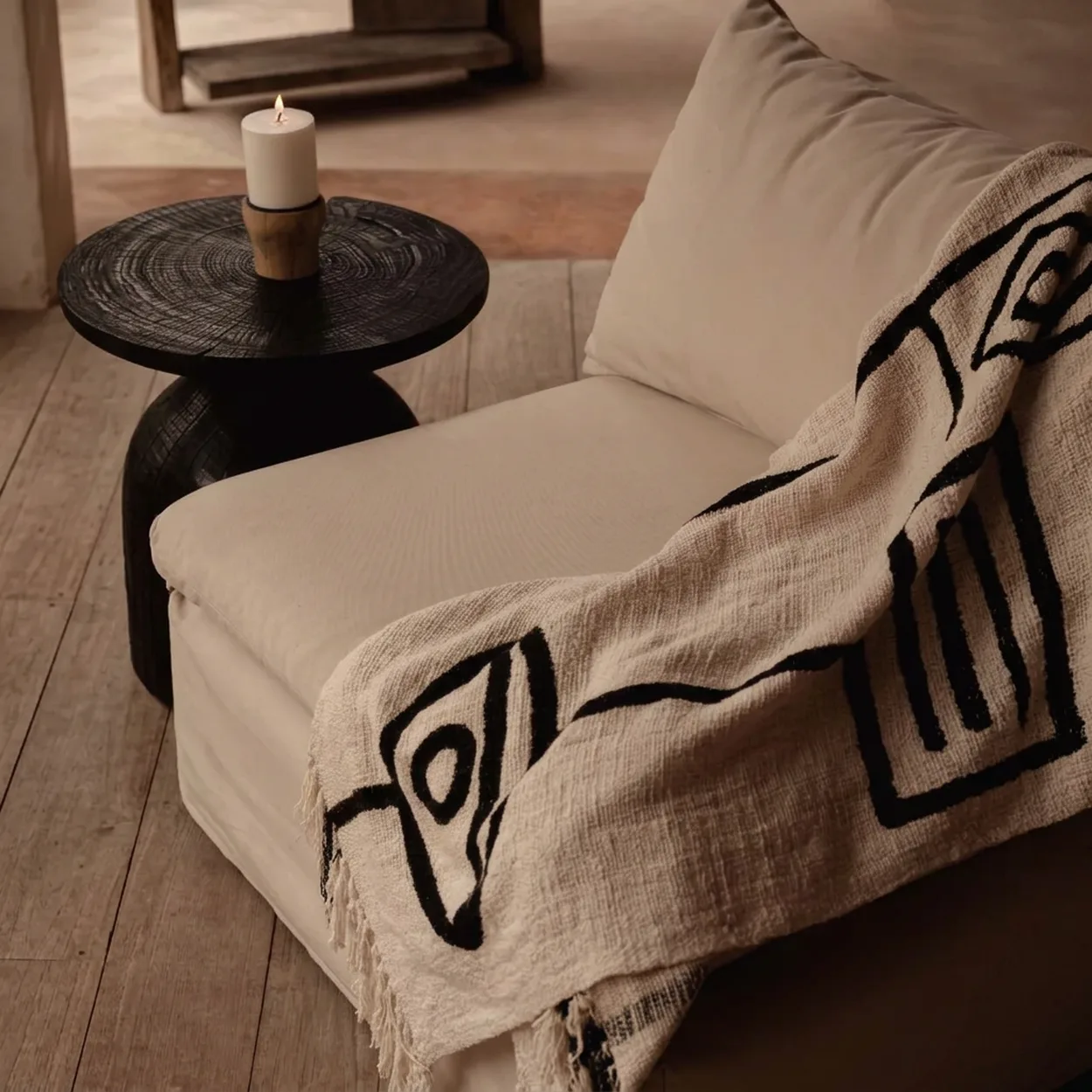 Cream lounge chair with a graphic woven throw beside a dark wood candle table