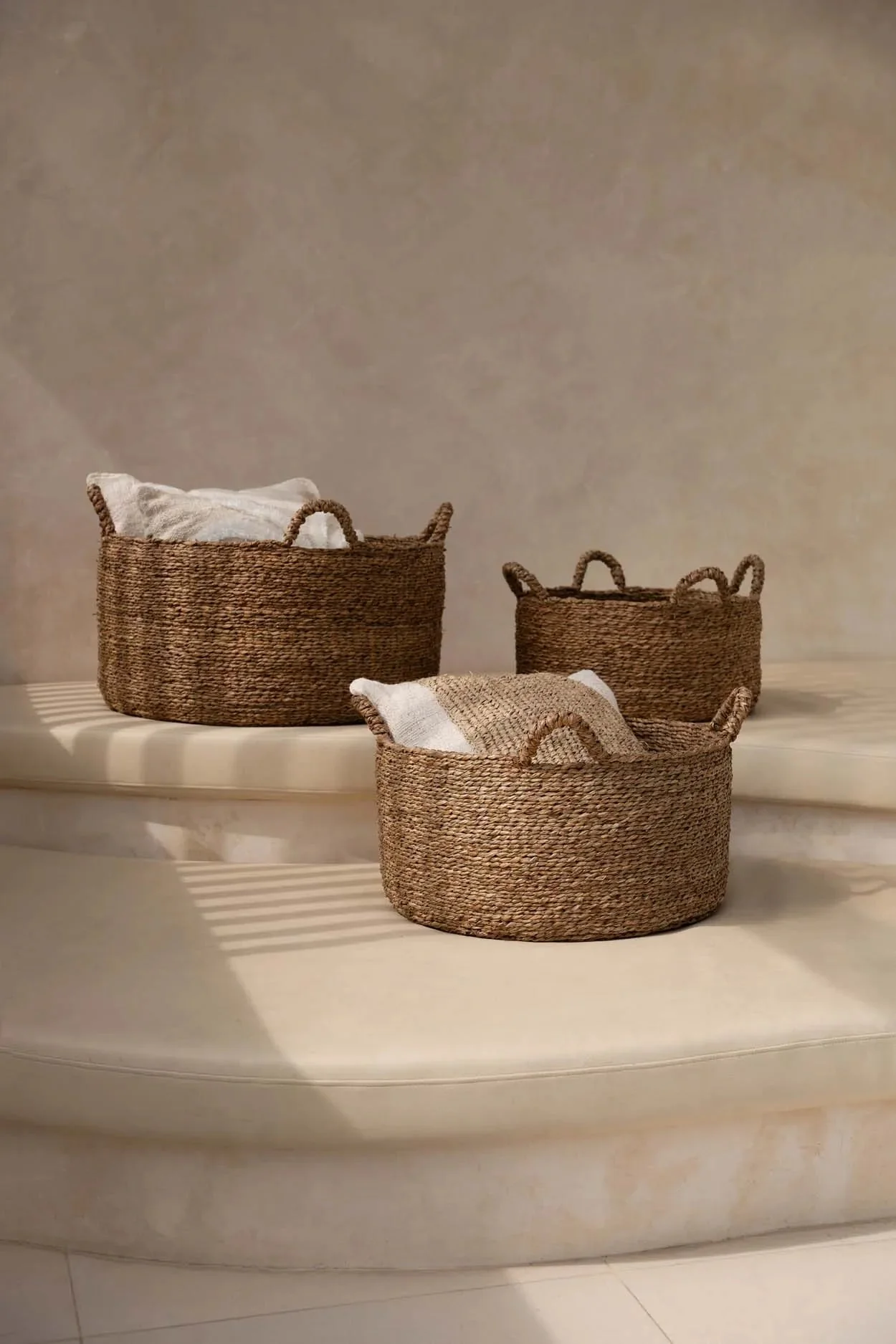 Three woven storage baskets with soft linens on sunlit stone steps