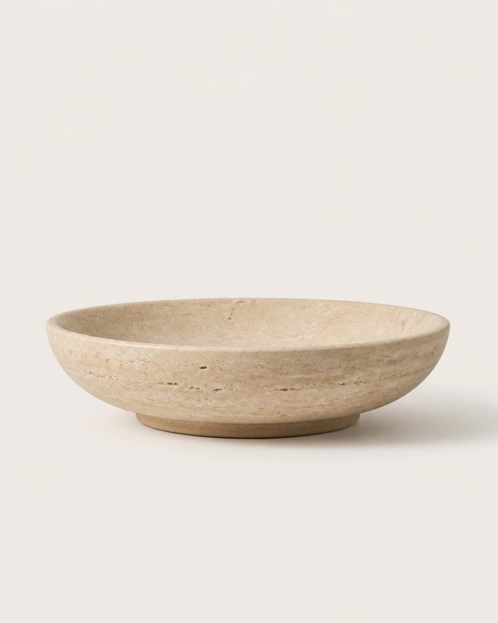 Shallow travertine stone bowl on a plain warm background