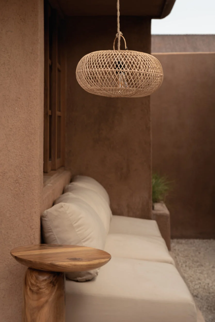 Woven rattan pendant lamp above a linen daybed on a warm terrace