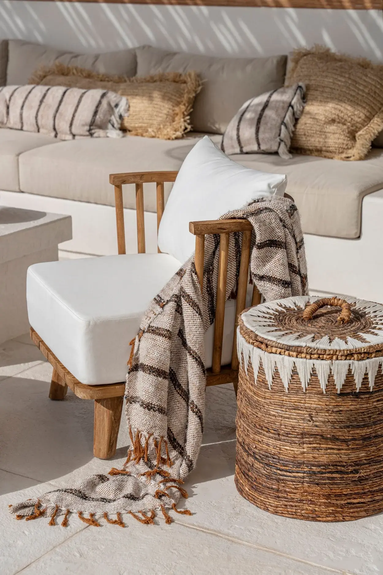 Striped fringed throw over a teak chair beside a woven storage basket