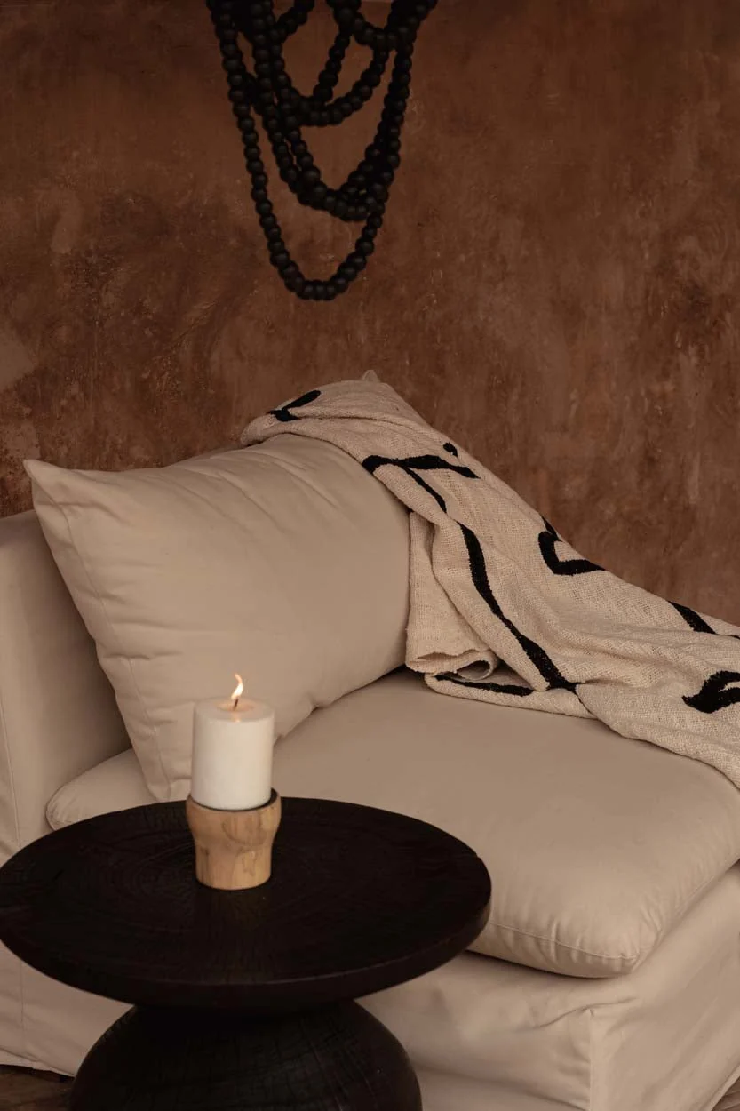 Lit pillar candle in a wooden holder on a dark round table by a sofa