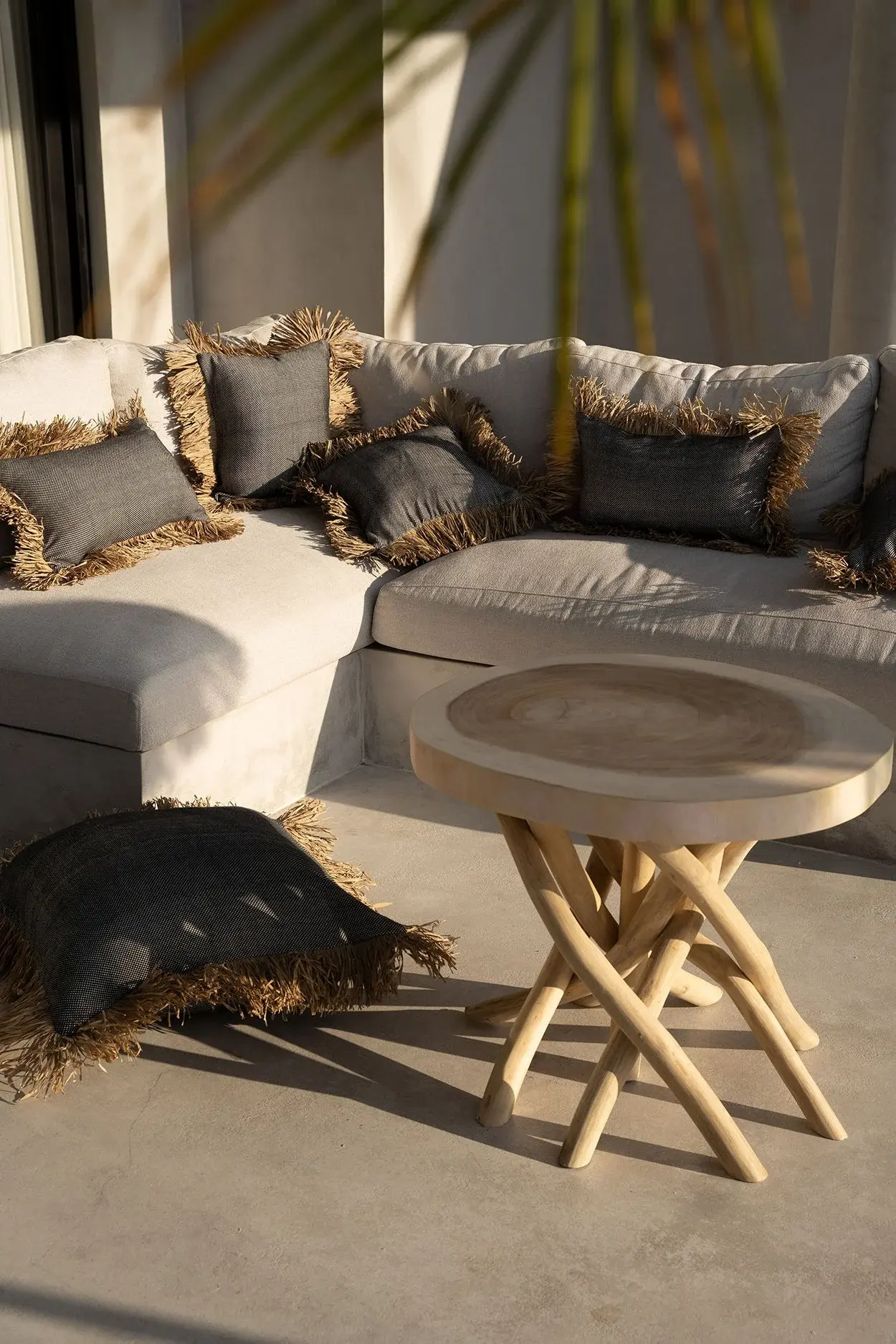 Sunlit outdoor lounge with fringed cushions and a sculptural wooden table